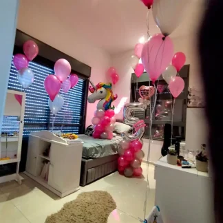 עיצוב חדר ליום הולדת בנושא חד קרן, זרי בלוני הליום בוורוד ובכסף ברחבי החדר, מעמד עם ראש חד קרן, בלון ספרה כסוף ובלון לב עם הדפסה אישית.
