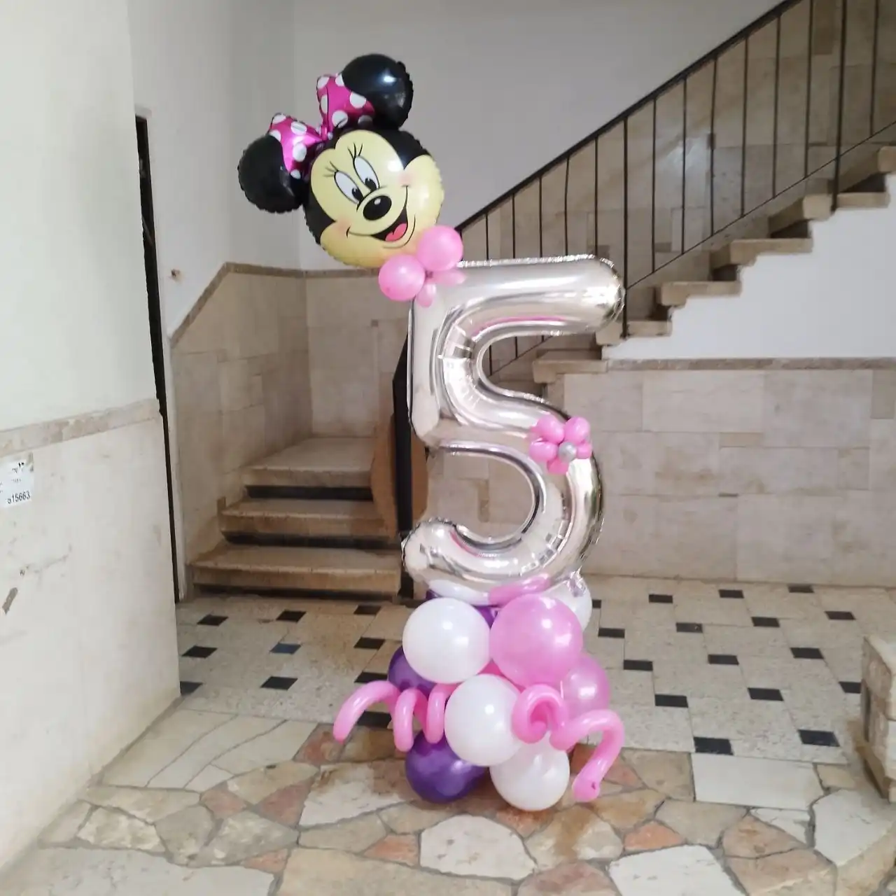 אותו מעמד בלונים מיני מאוס עומד על רצפת חדר מדרגות, לפני מסיבת יום הולדת.